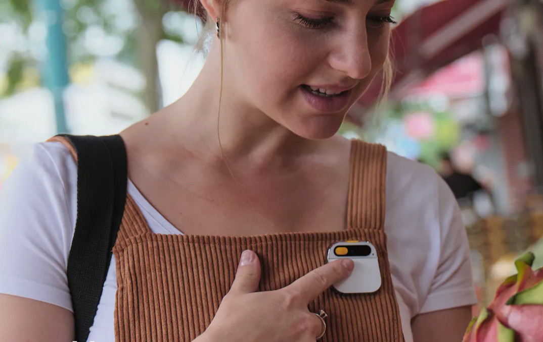 An image of a woman touching a small, square electronic device that is attched to her overalls